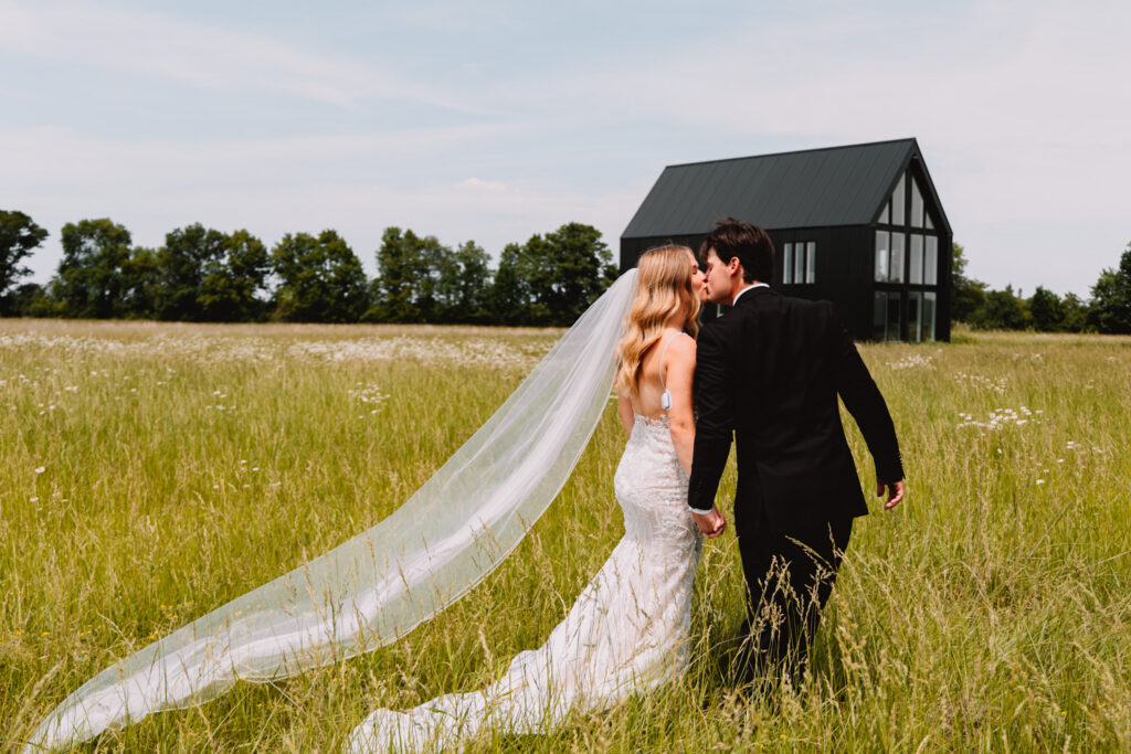 Couple in field at Ivory North Co in front of NorthHaus with brides veil drooping in wind