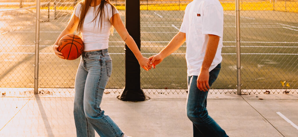 couple holding hands walking playing basketball at golden hour in minnesota